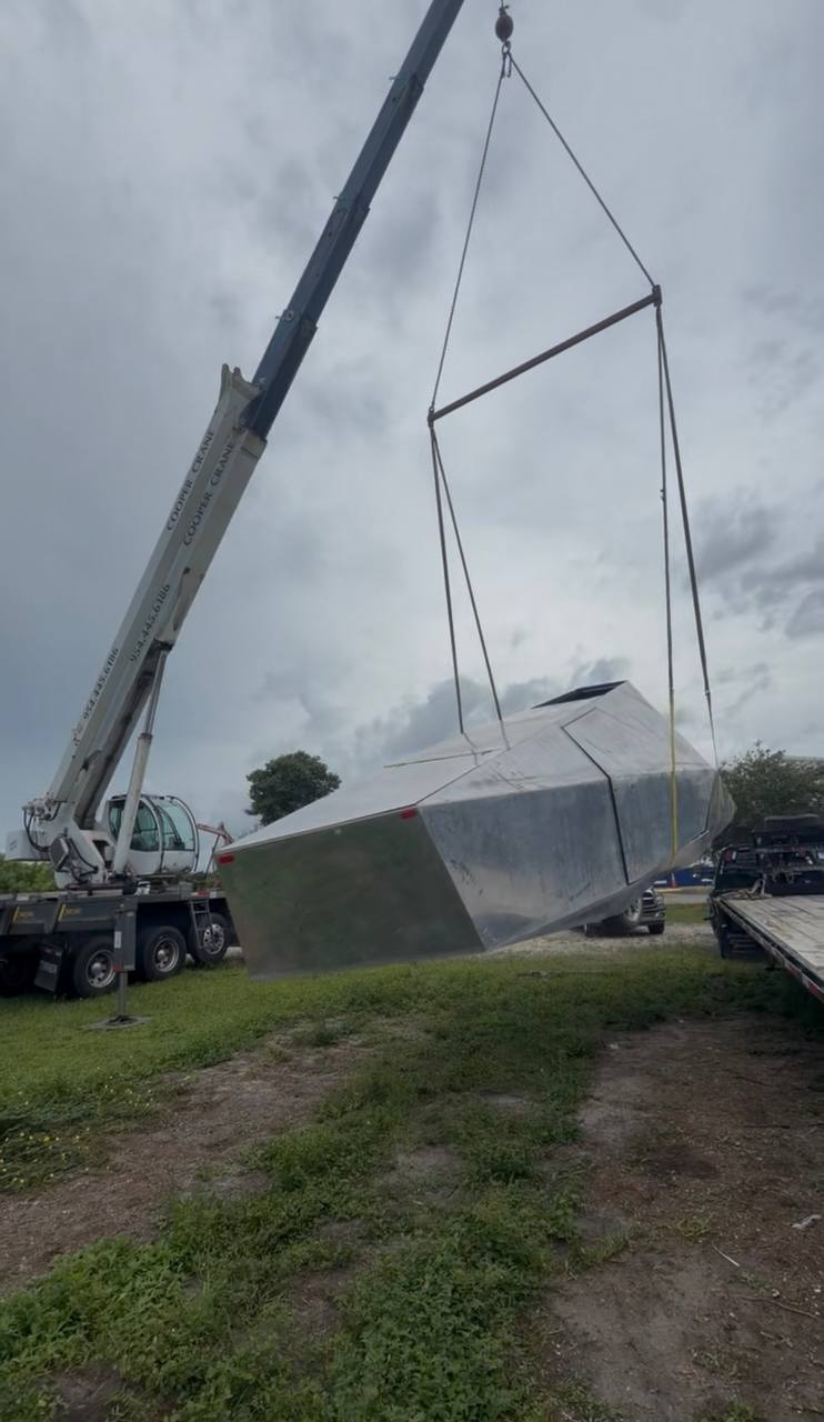 Stainless Cybertruck body rigged and lifted off a flatbed trailer by a Cooper Crane crane