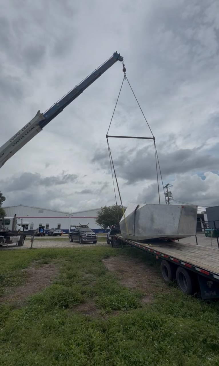 Cybertruck body hanging from a Cooper Crane boom above a flatbed trailer