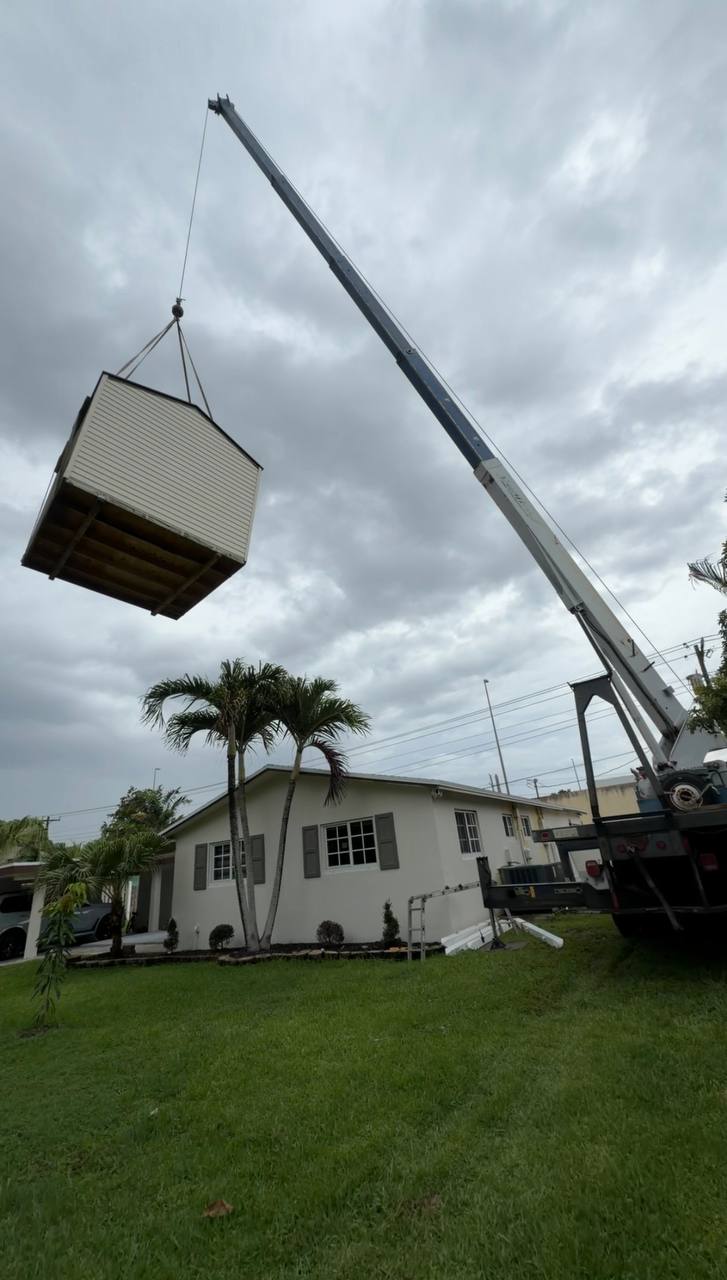 Cooper Crane boom truck lifting a storage shed into a Southeast Florida backyard