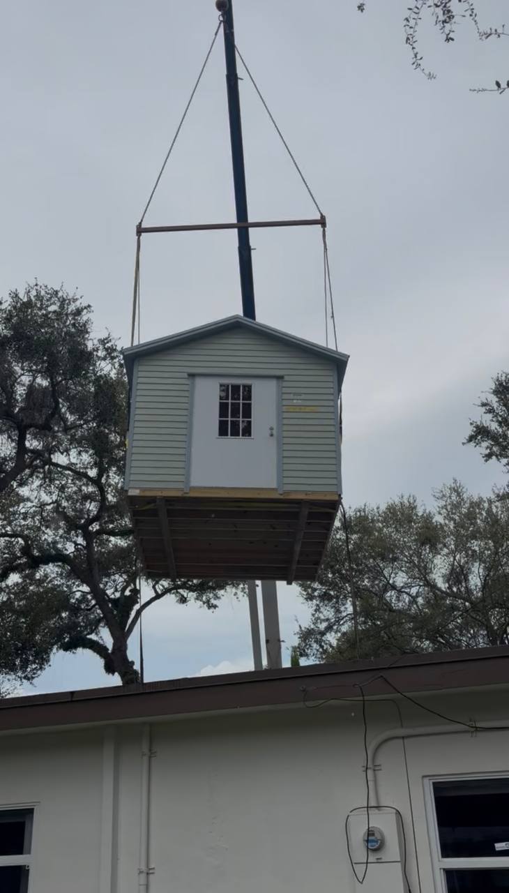 Storage shed hanging from a Cooper Crane boom over the roof of a house