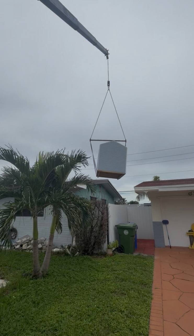 Small shed lifted over a fence into a side yard by a Cooper Crane boom truck