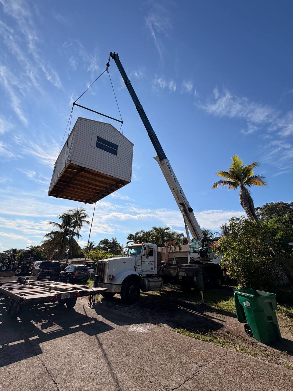Cooper Crane boom truck lifting a shed off a delivery trailer on a residential street